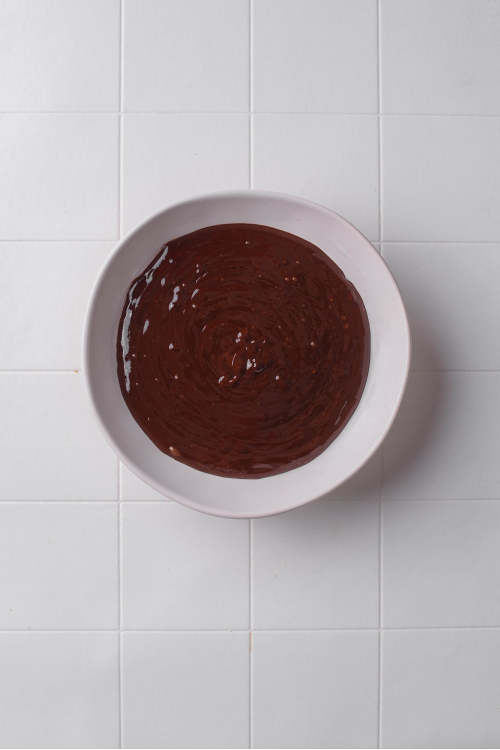A white bowl with melted chocolate on a tiled counter.