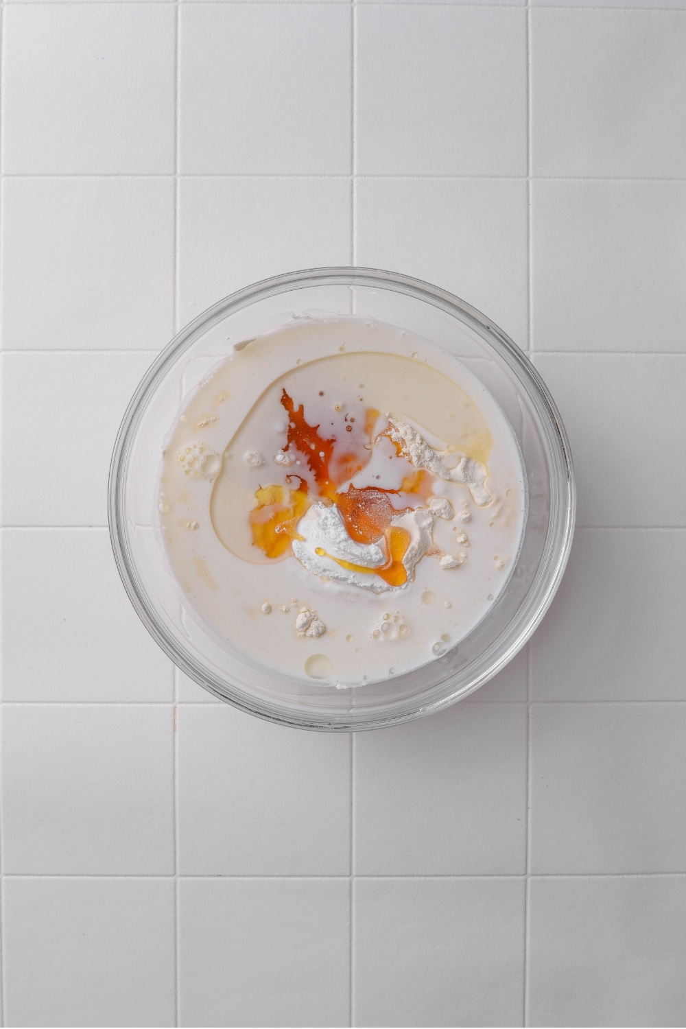A glass bowl with coconut milk, coconut oil, and sugar free syrup on a tiled counter.