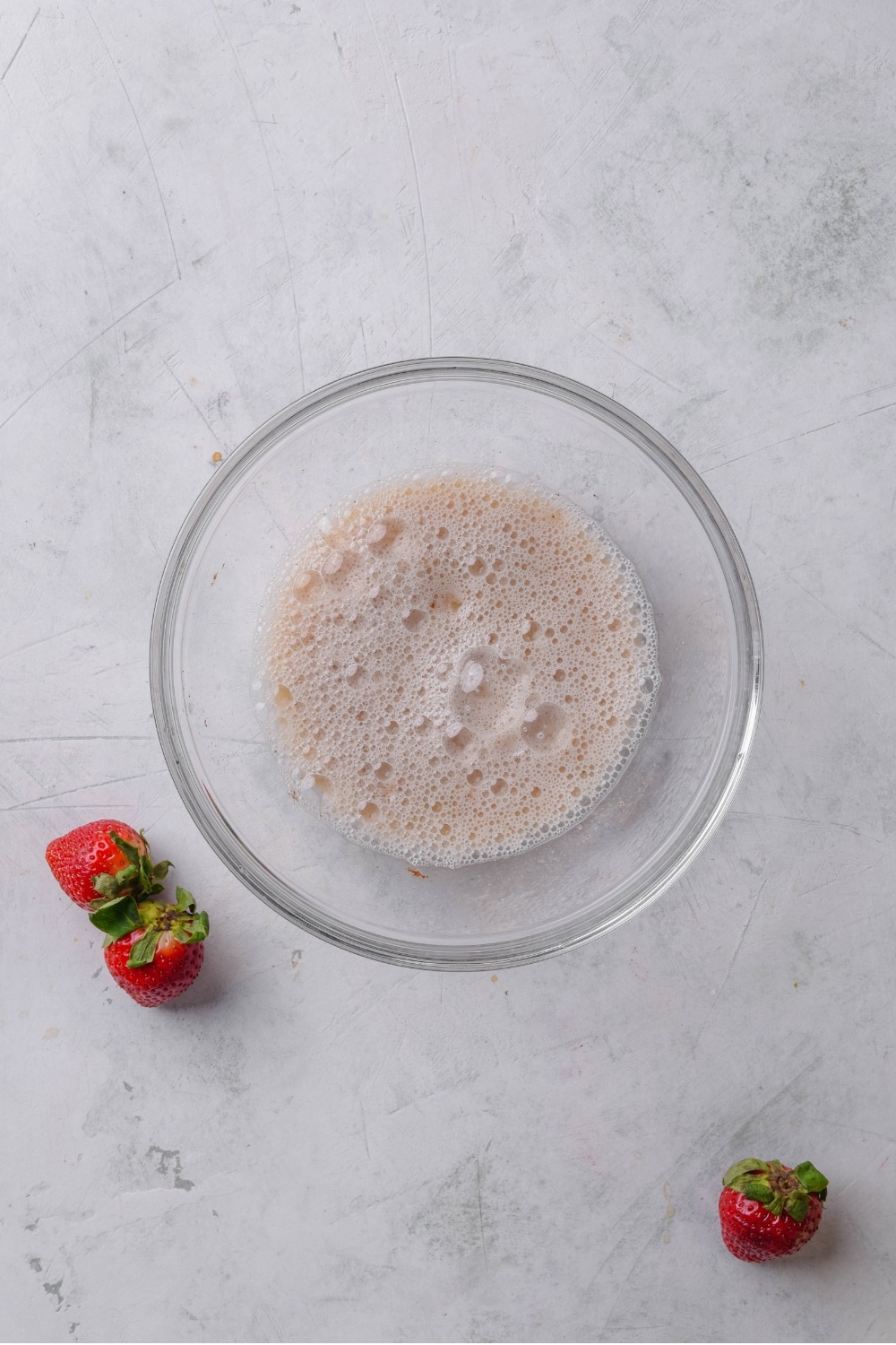 An overhead shot of a glass bowl on a marble counter. The bowl has whisked egg and milk mixture