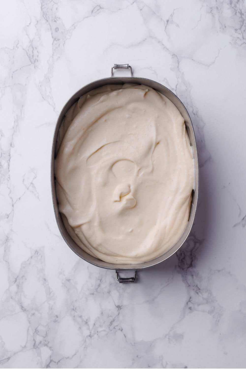 A metal loaf pan with a frozen vanilla protein ice cream mixture spread evenly.