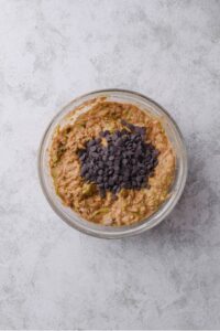 A glass bowl filled with zucchini bread batter with chocolate chips on top.