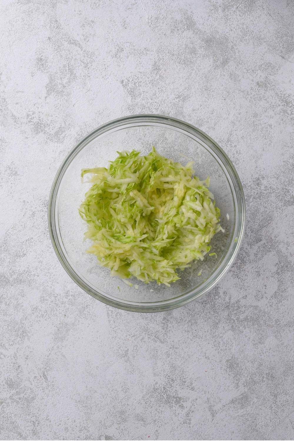 A glass bowl filled with shredded zucchini.