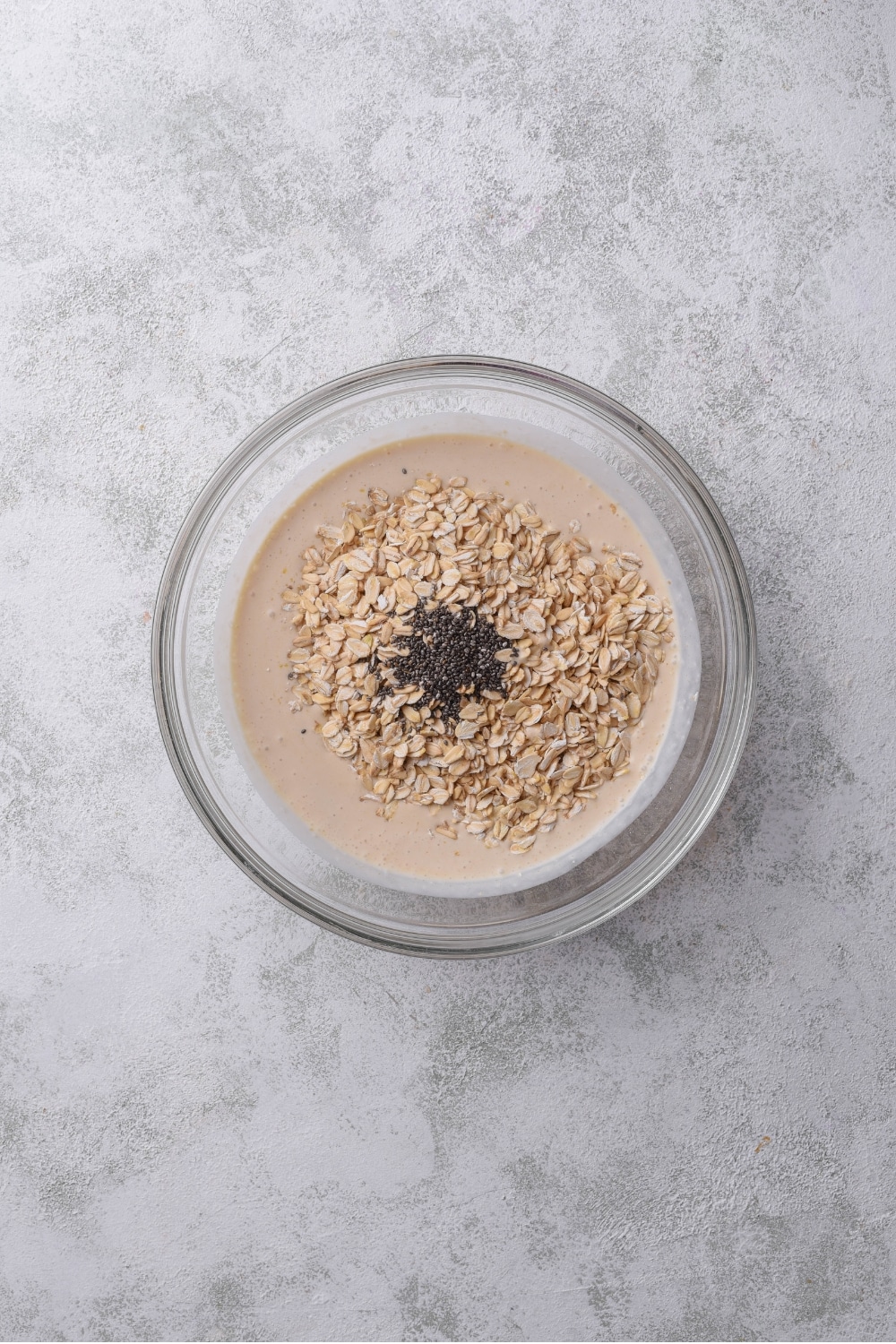 A glass bowl filled with a milk and yogurt mixture, with oats and chia seeds on top.