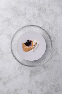 An overhead shot of a glass bowl filled with almond milk, peanut butter, and chocolate sauce.