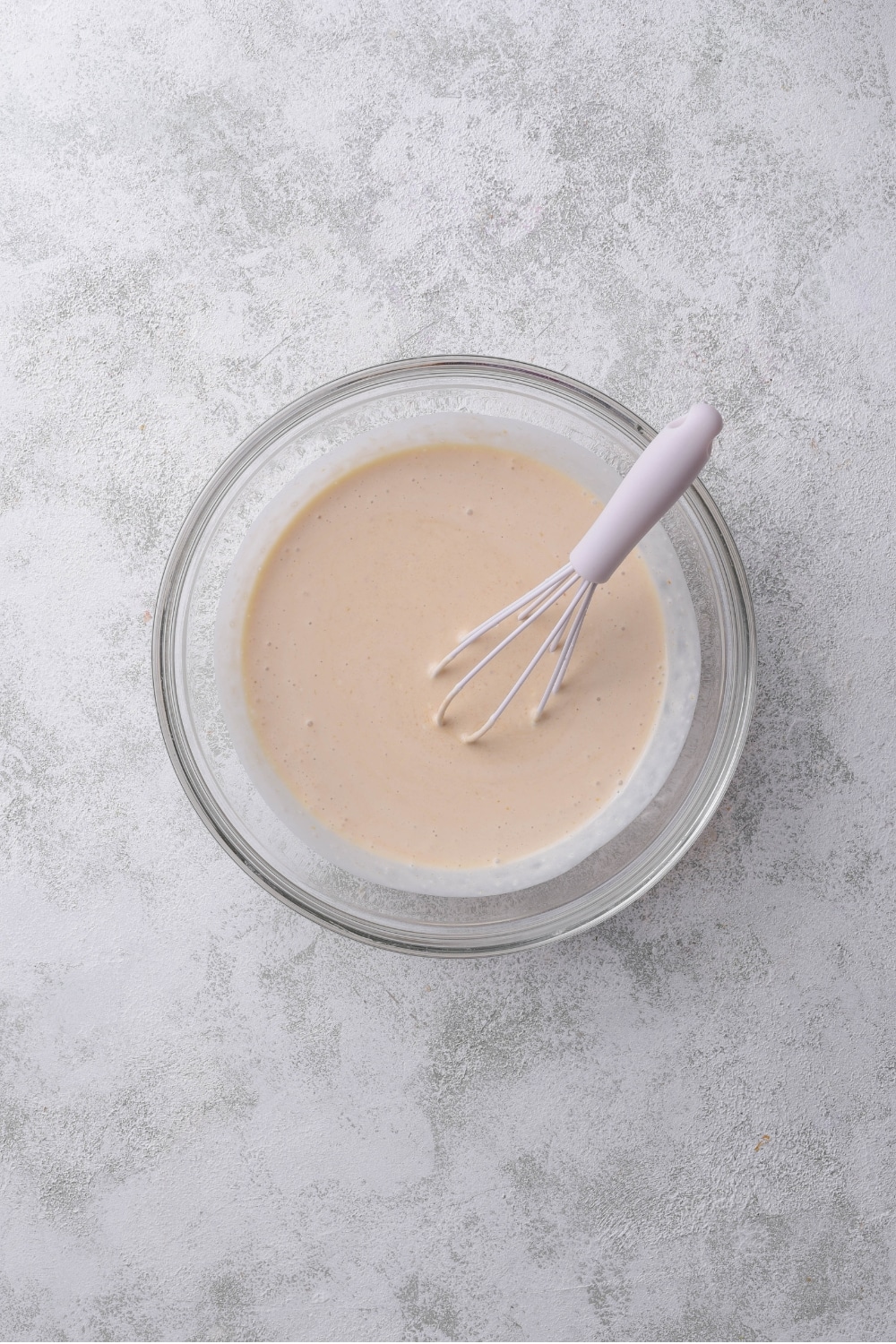 An overhead shot of a glass bowl filled with an almond milk, peanut butter, and greek yogurt mixture. There is a whisk in the bowl.