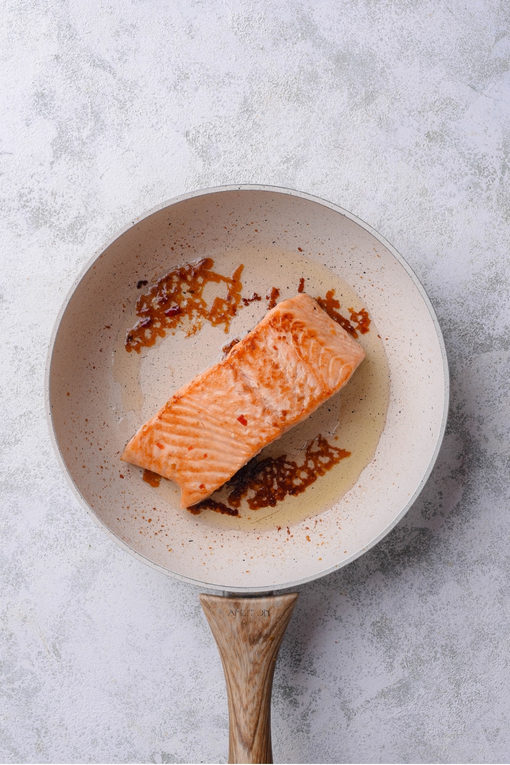 A ceramic skillet with salmon cooking in olive oil.