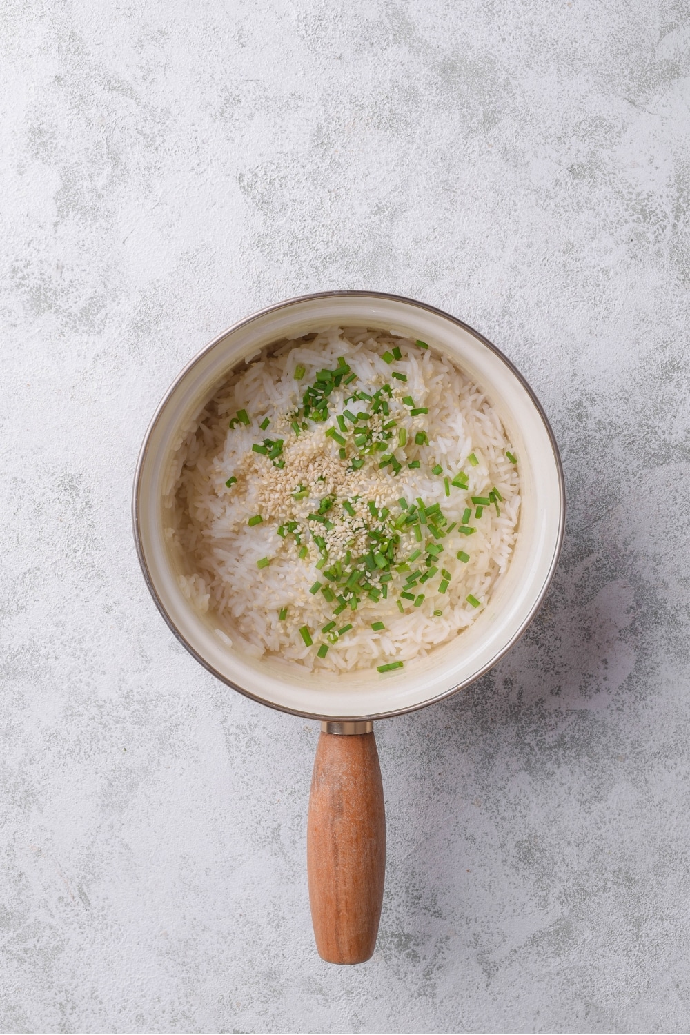 A stove pot with white rice and chopped chives cooking in water.