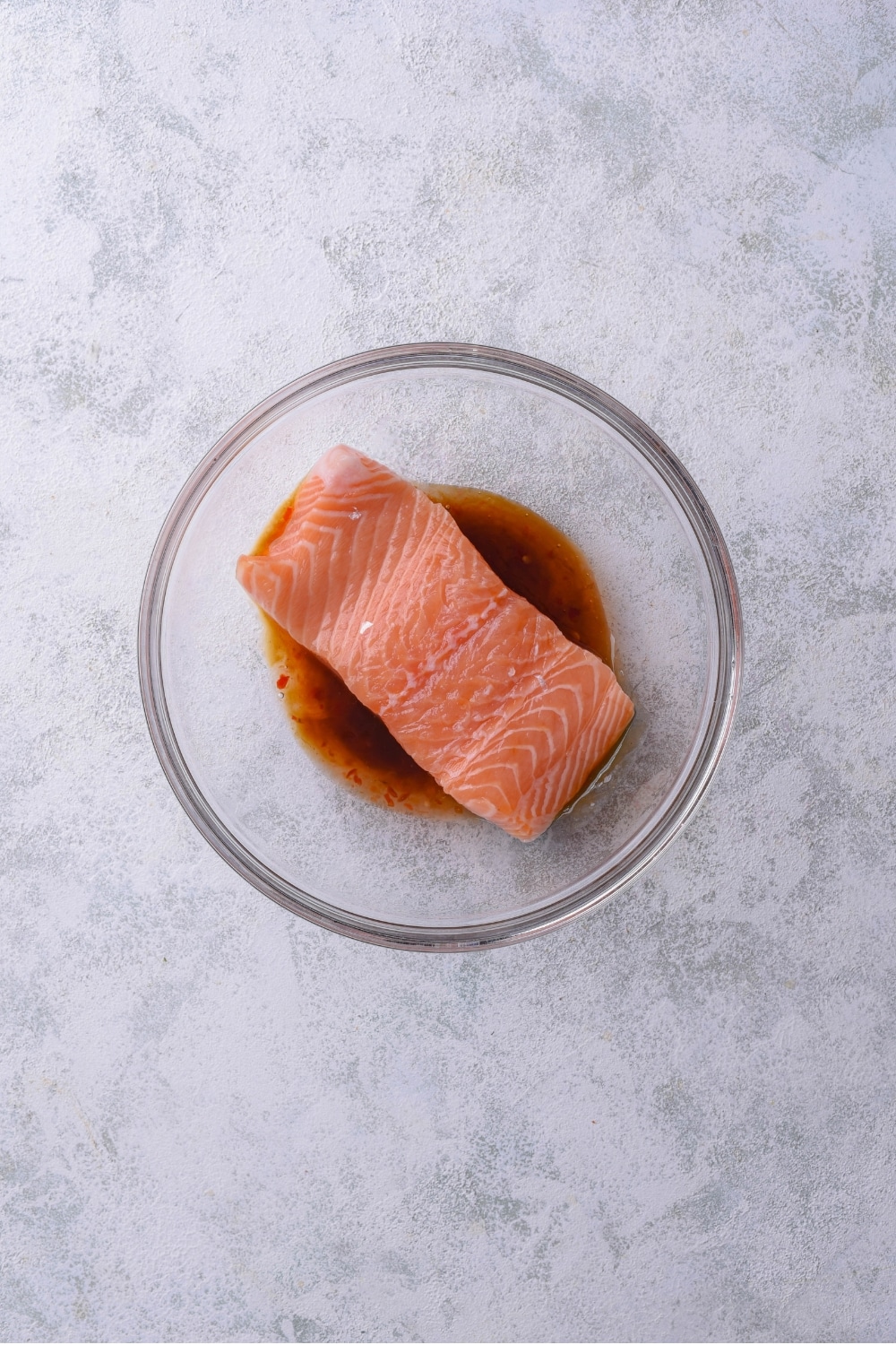 A glass bowl with a salmon fillet marinating in teriyaki sauce.