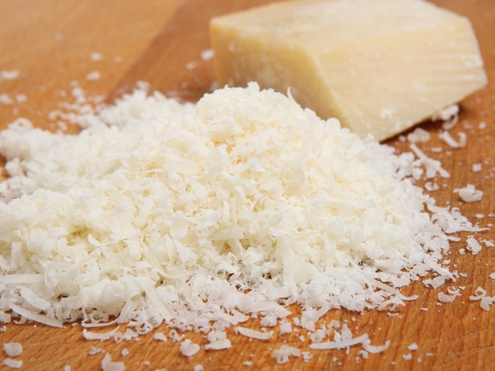 A pile of grated parmesan cheese on a woodedn cutting board.