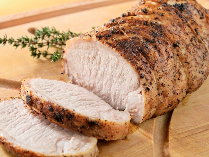 A whole pork tenderloin that is sliced with two pieces in front of it.