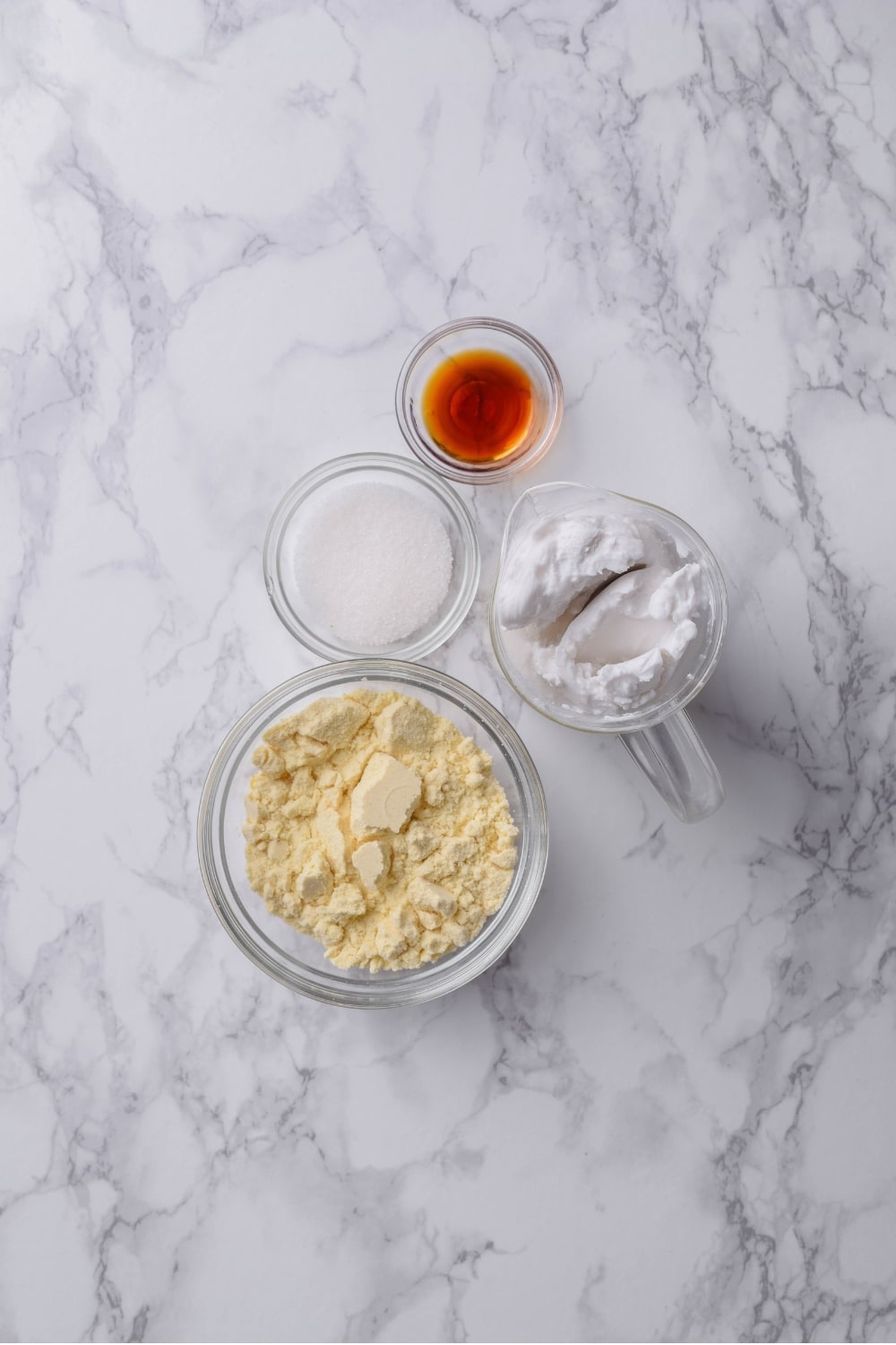 Four glass bowls of various sizes filled with vanilla protein powder, coconut milk, sugar, and vanilla.