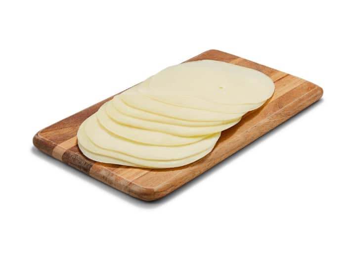 A bunch of slices of provolone cheese on a wooden cutting board.