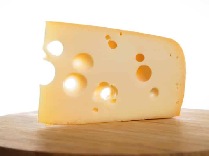 A block of swiss cheese on a wooden board.