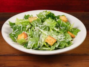 A caesar salad with croutons in a white bowl.