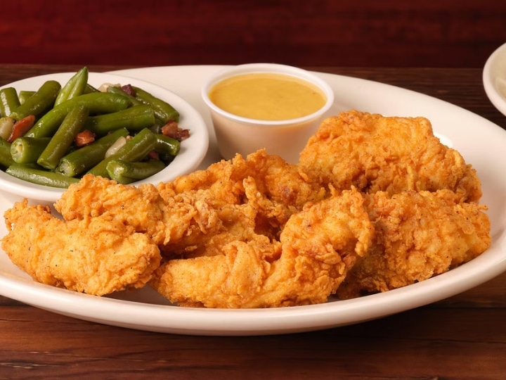 A bunch of fried chicken on a plate with green beans and honey mustard.