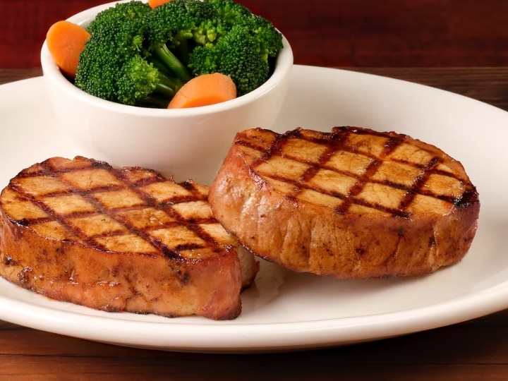 Two grilled pork chops with a bowl of broccoli on a white plate.