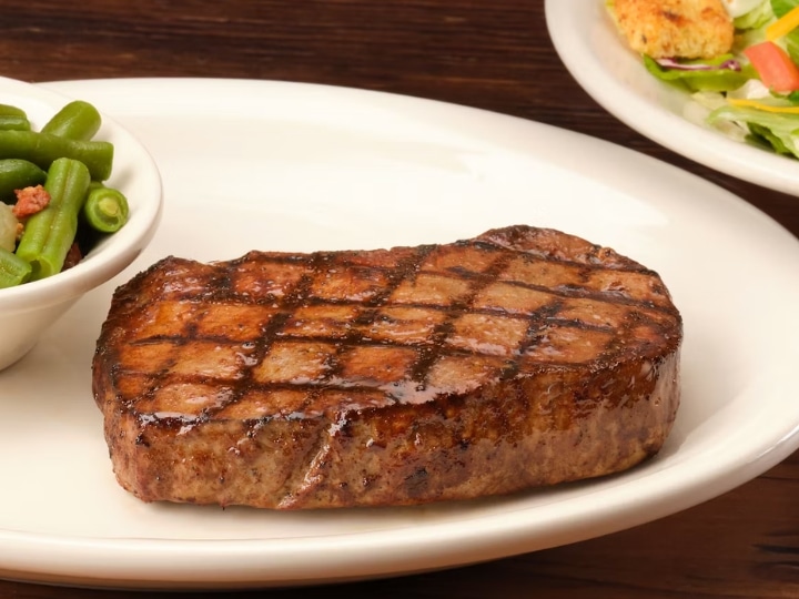 A piece of steak on a white plate with a bowl of green beans.