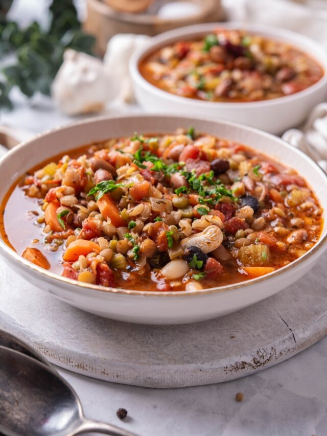 A bowl of bean soup in a ceramic soup bowl on a wooden serving board. There is another bowl of soup in the background.