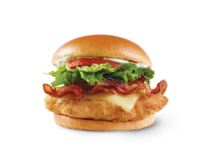 A crispy chicken sandwich with cheese, bacon, lettuce, tomato, and sauce.