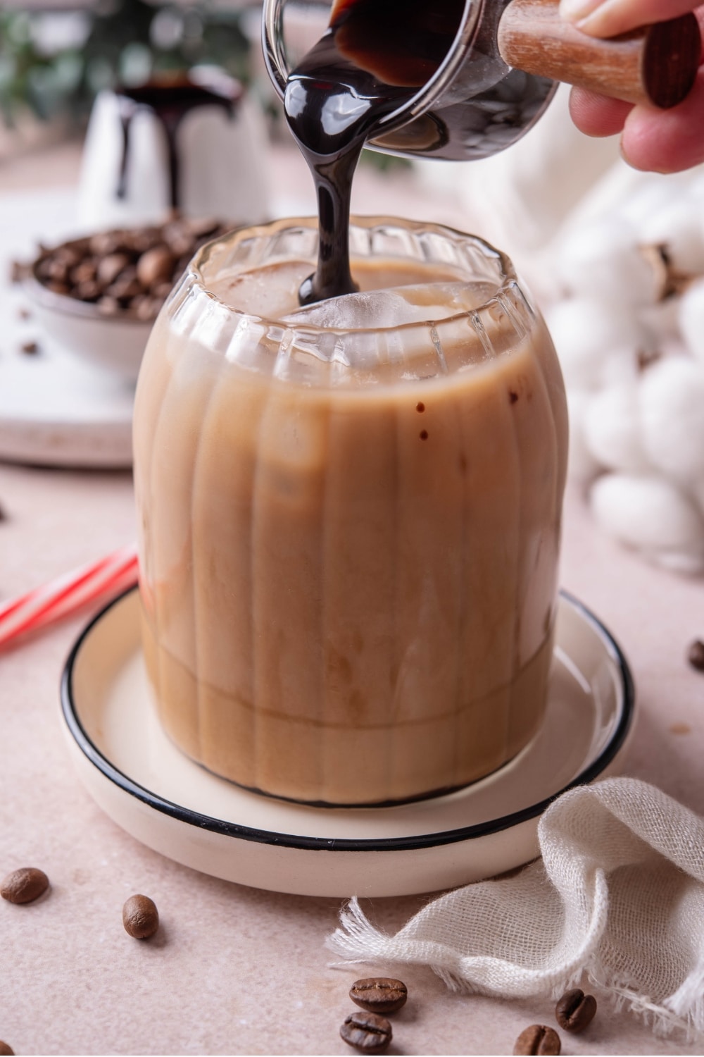 A ribbed glass of low calorie iced coffee on a ceramic saucer with chocolate sauce being poured into the glass.