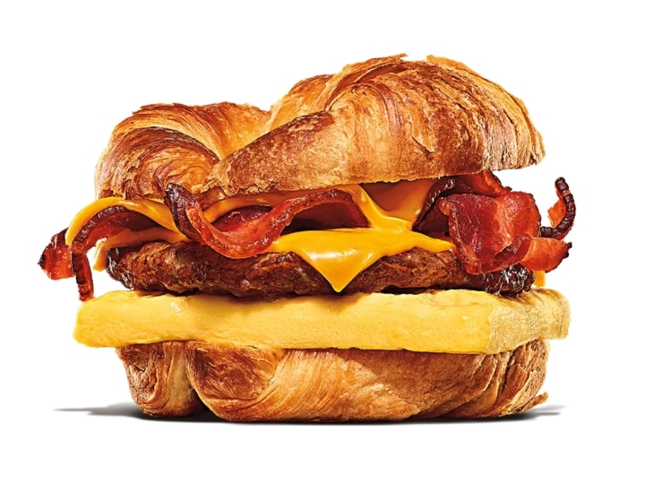 A croissant with bacon, cheese, sausage, and an egg.