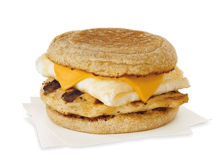 An english muffin sandwich with an egg white, slice of cheese, and piece of grilled chicken.