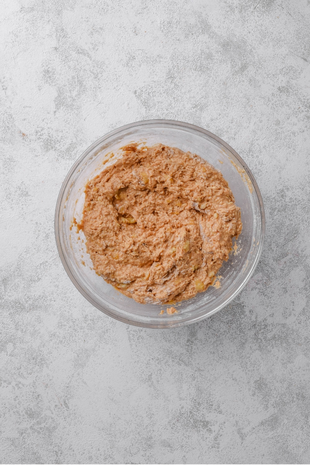 An overhead shot of a glass bowl filled with a banana batter mixture.