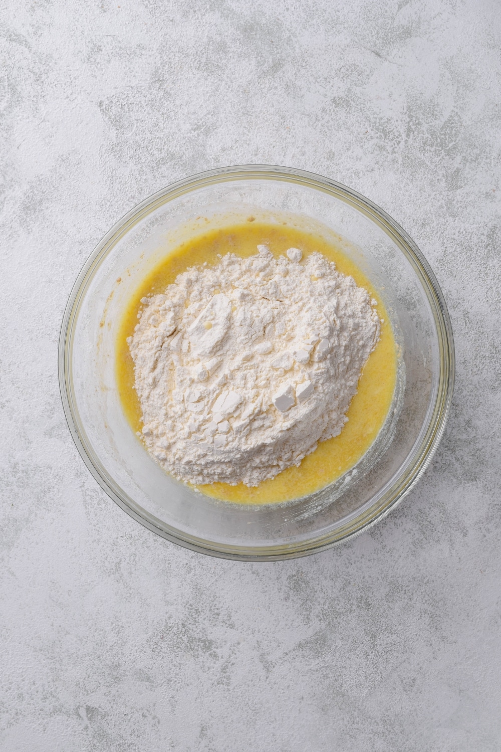 An overhead shot of a glass bowl filled an oat and egg mixture with flour on top.