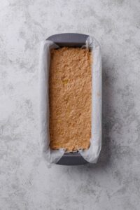 An overhead shot of a raw loaf of banana bread in a loaf pan lined with parchment paper.