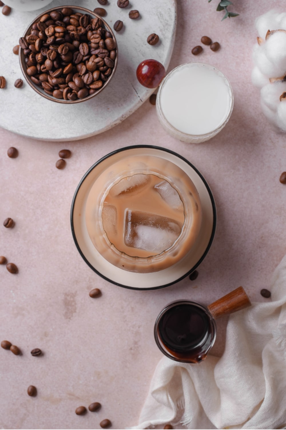 An overhead shot of a glass of low calorie iced coffee. The glass is filled with ice cubes and iced coffee, with a saucer of milk and serving of chocolate sauce next to the glass.