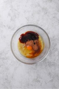 An overhead shot of a glass bowl filled with mashed banana, egg, egg white, vanilla, and cinnamon.