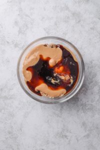An overhead shot of a glass bowl with peanut butter and syrup poured on top of an oat mixture