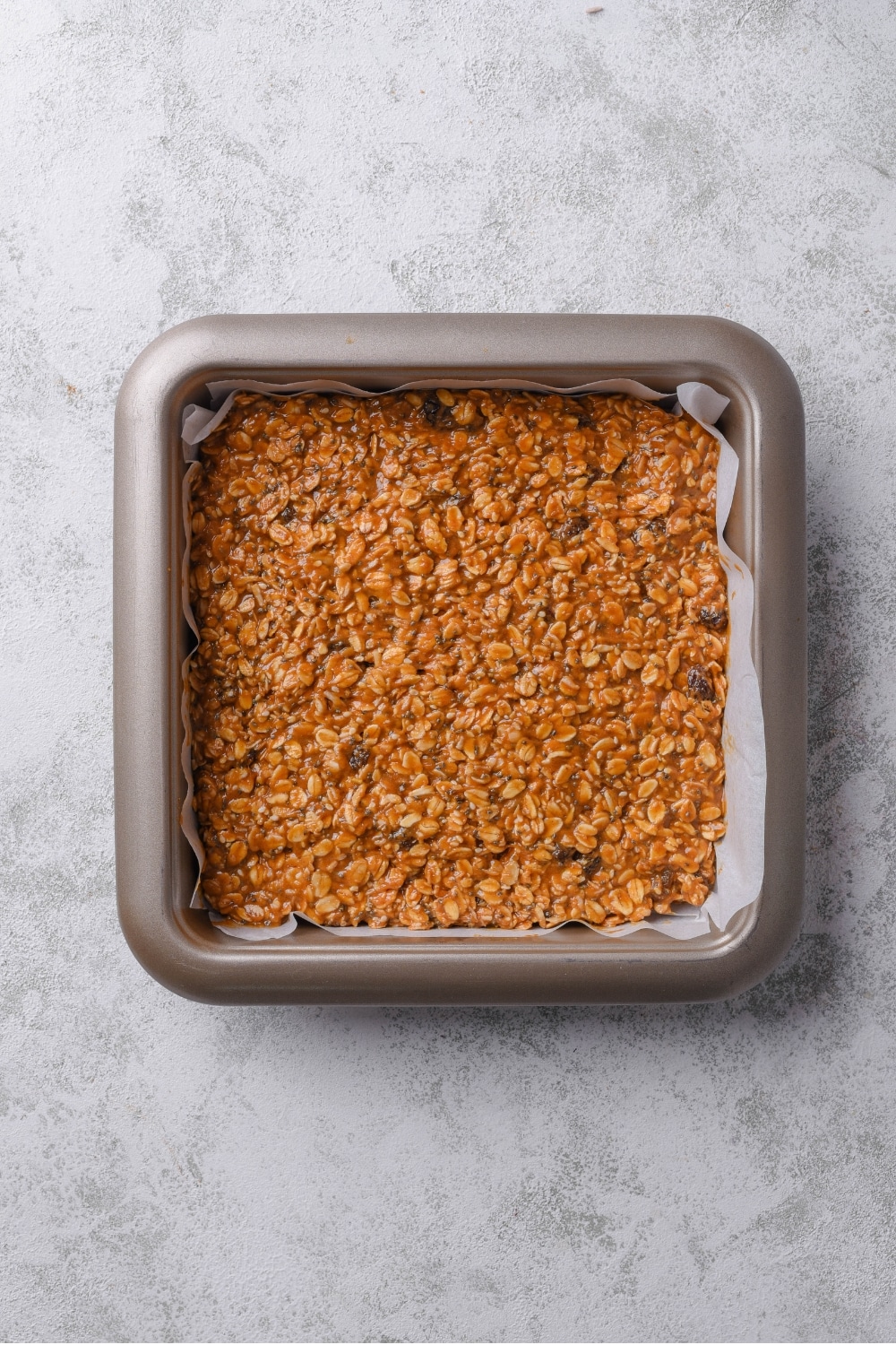 An overhead shot of a baking pan lined with parchment paper filled with an uncut energy bar mixture