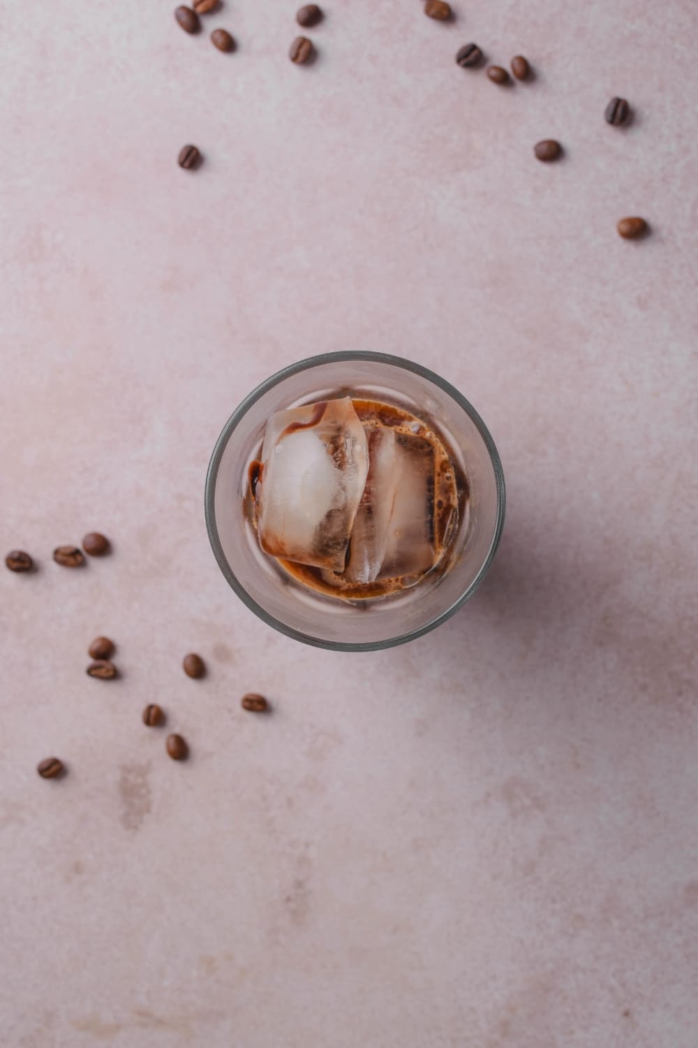 An overhead shot of a glass filled with coffee, milk, chocolate sauce, and vanilla with iced cubes on top.