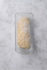 An overhead shot of raw oat dough in a loaf pan wrapped in plastic wrap
