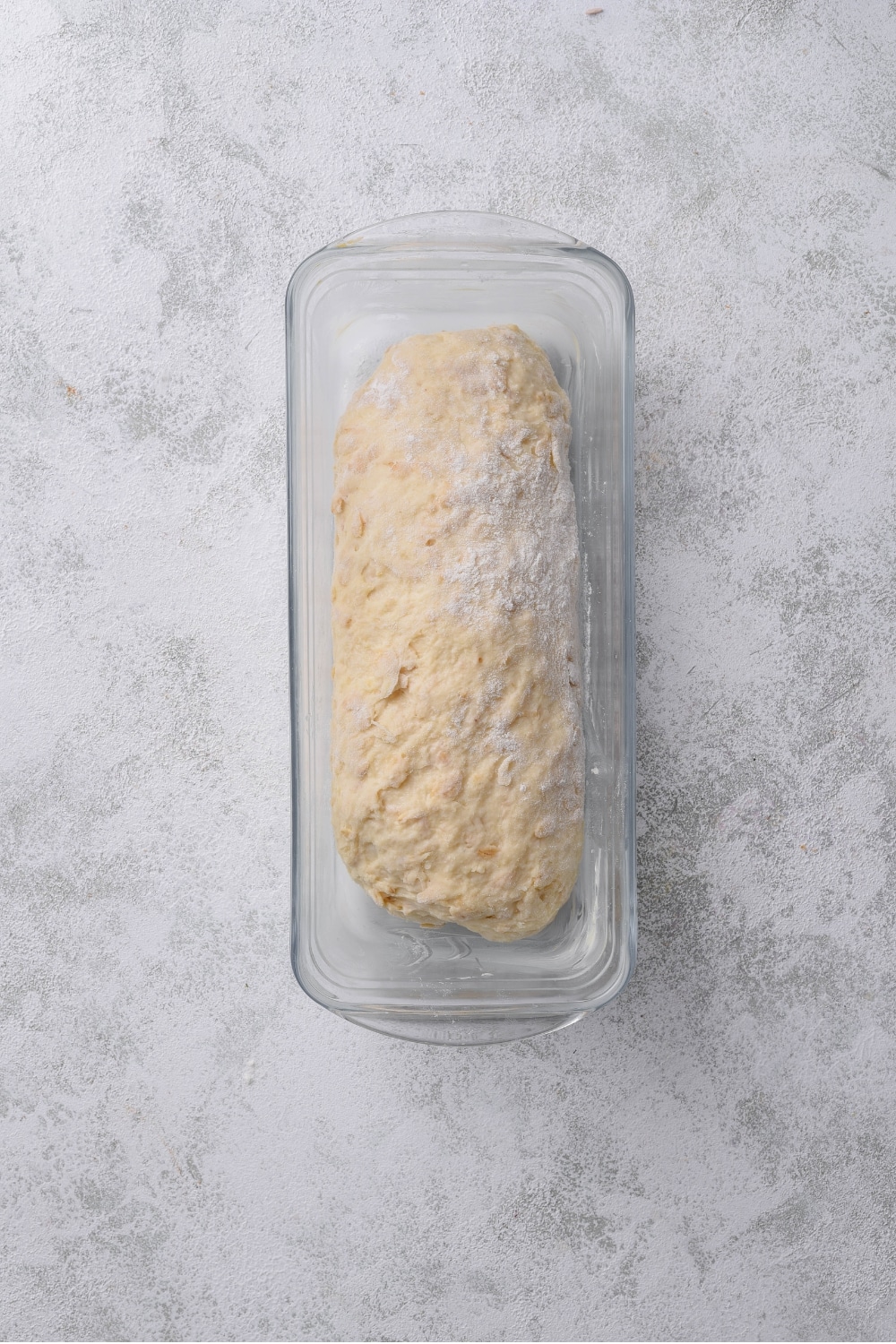 An overhead shot of raw oat dough in a loaf pan wrapped in plastic wrap