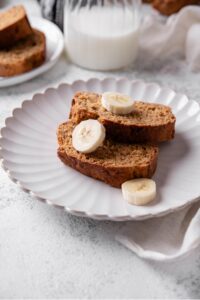Two slices of low calorie banana bread served on a white ceramic plate with three slices of banana served on the bread.