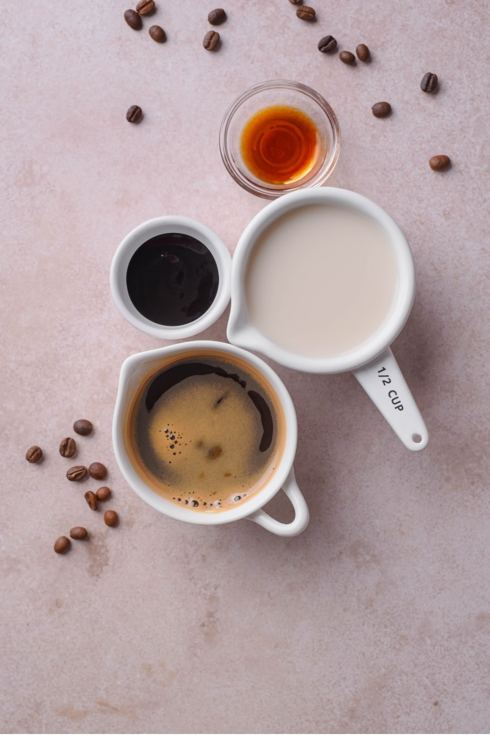 An overhead shot of several ingredients to make low calorie iced coffee in a variety of bowls, including coffee, vanilla, almond milk, and chocolate sauce.