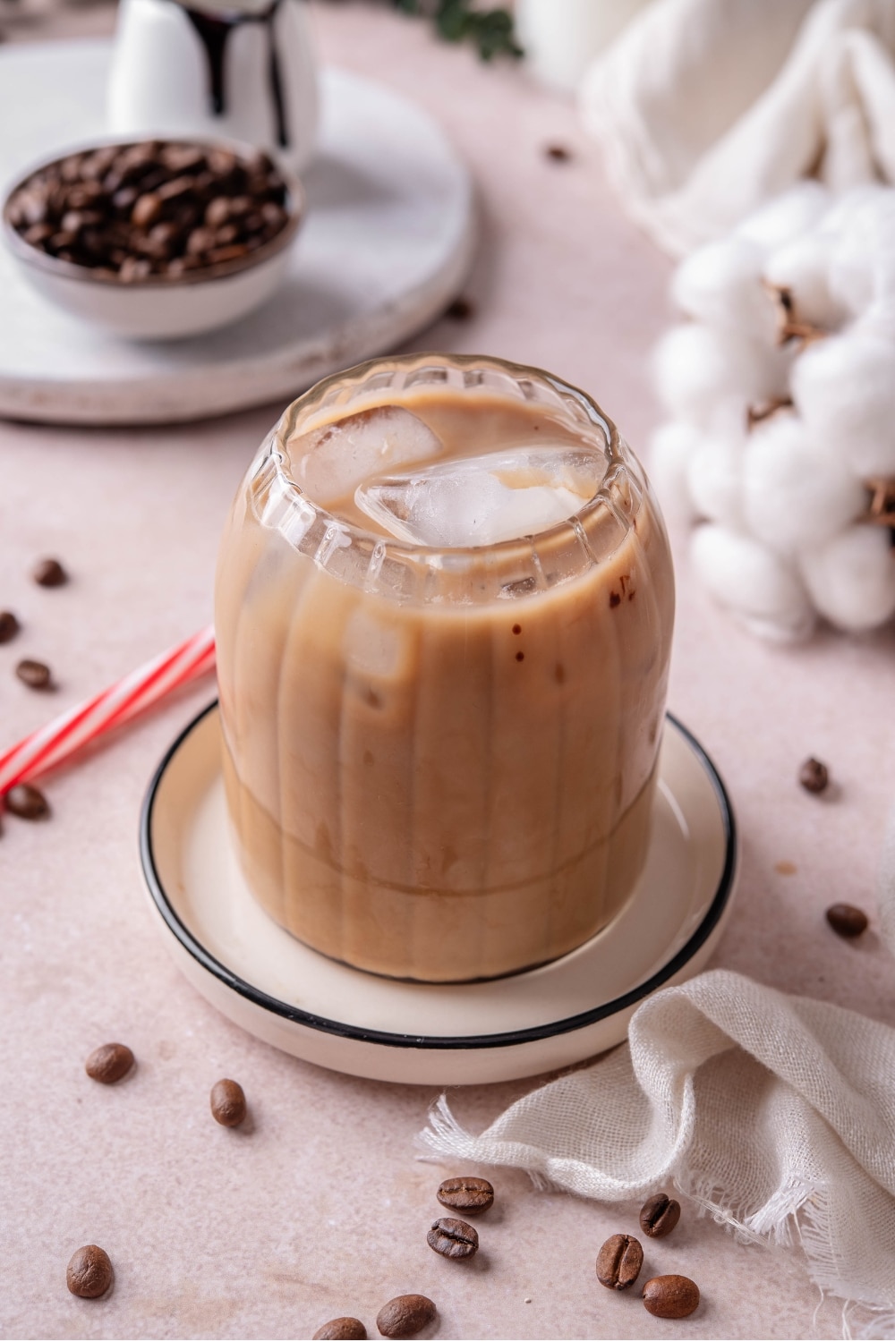 A ribbed glass filled with low calorie iced coffee on a ceramic saucer with a red and white striped straw next to the glass.