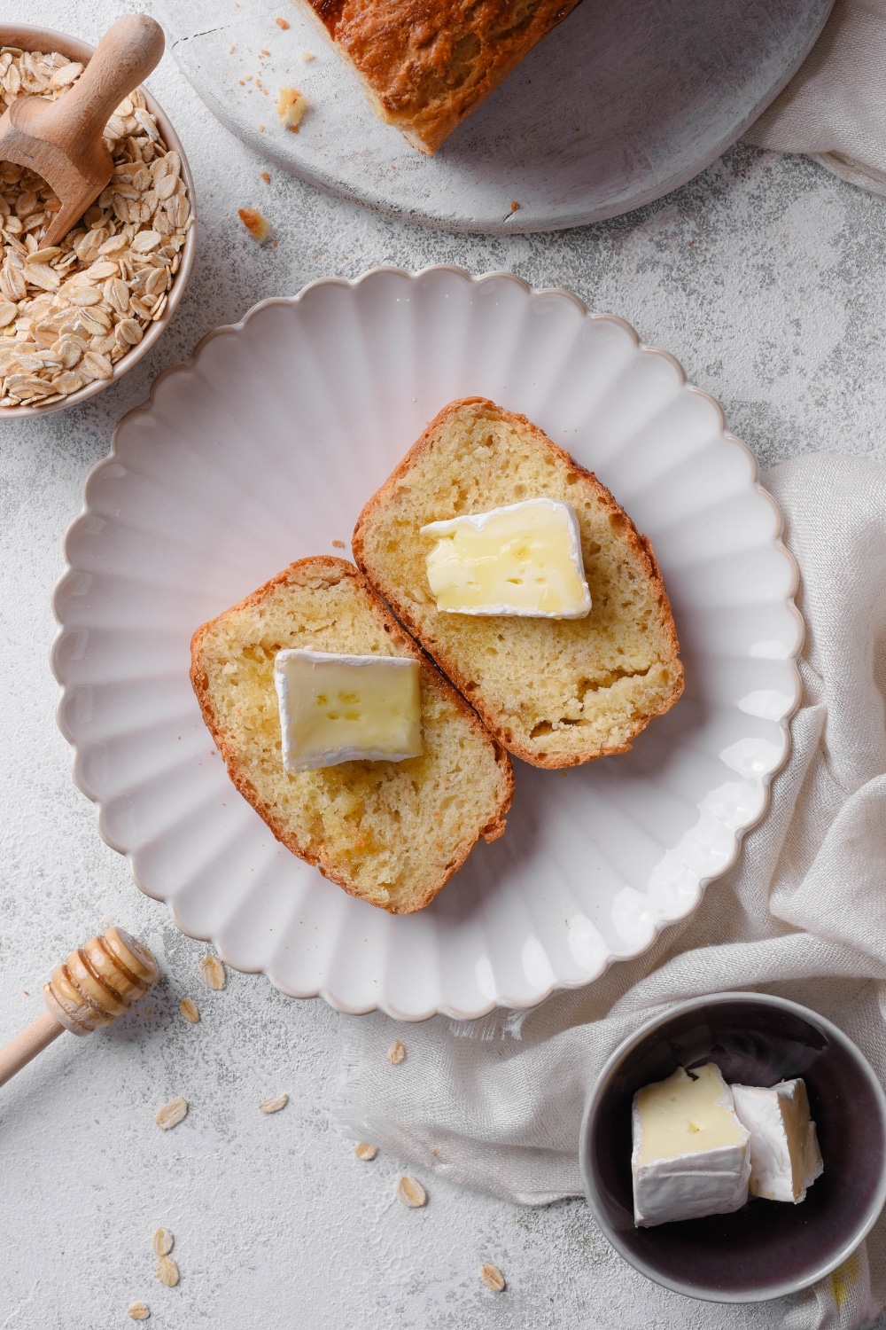 An overhead shot of two slices of oat bread on a white ceramic plate topped with butter and drizzled with honey.