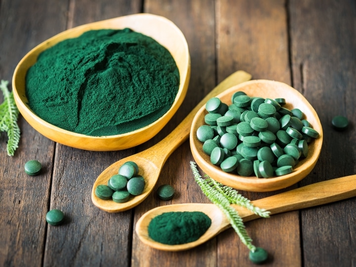 a bowl of spirulina, a bowl of spirulina seeds, and two wooden spoons of spirulina.