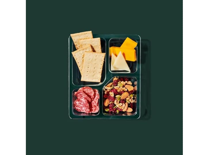 A box with cheddar, salami, a nut mix, and crackers.