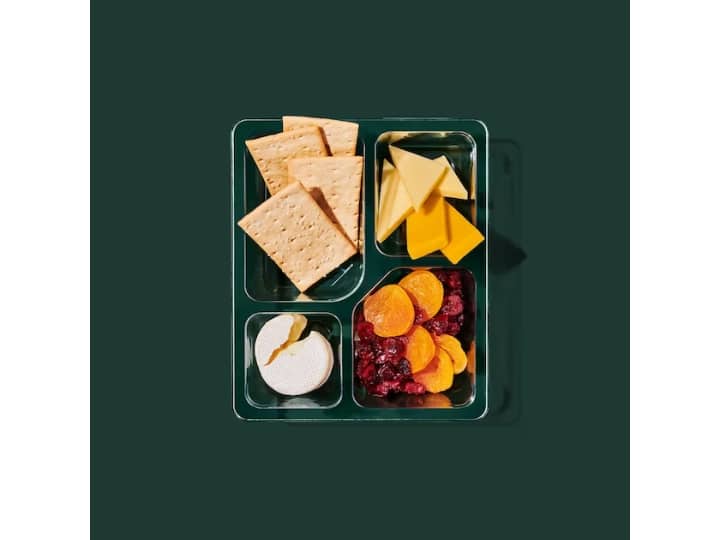 A box with sliced cheese, a gouda cheese wheel, crackers, and dried fruit.