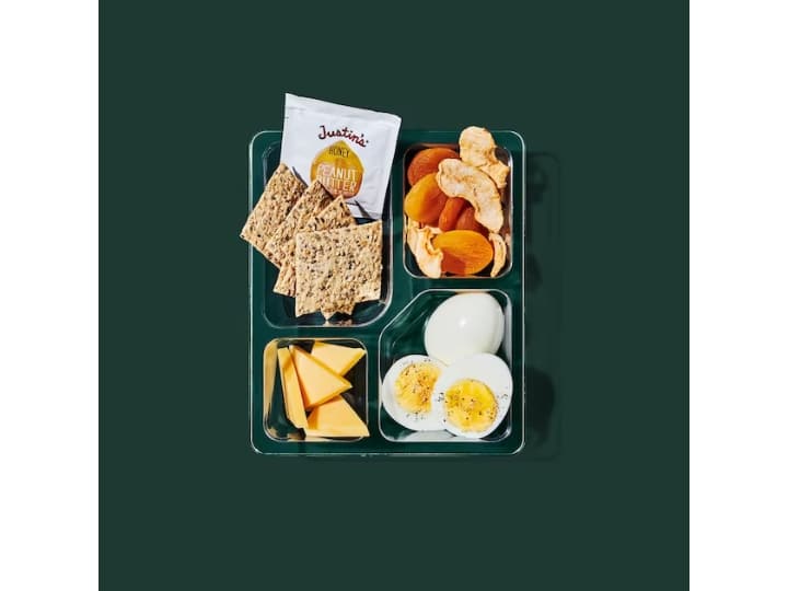 A box with crackers, sliced apples, sliced hard boiled eggs, and cheese.