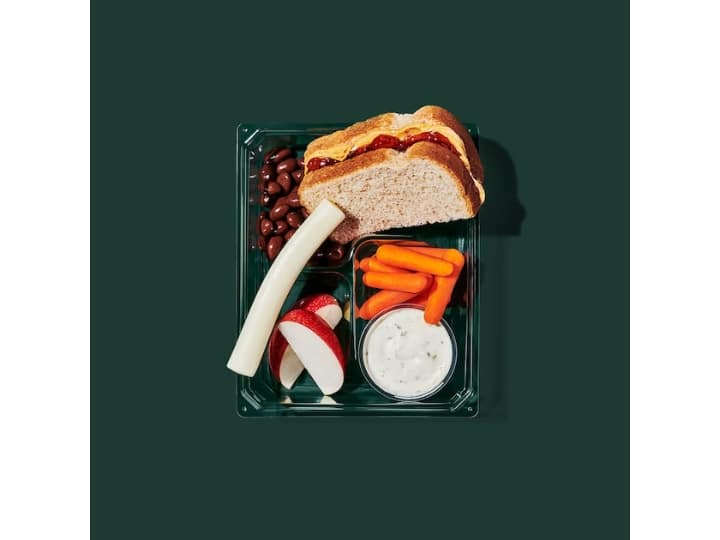 A box with a peanut butter and jelly sandwich, string cheese, apple slices, carrots, and ranch.