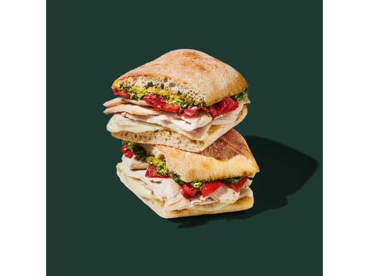 A turkey sandwich with pesto, peppers, and cheese on a ciabatta bun.