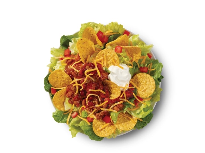 Tortilla chips and bacon with cheese and sour cream on top of lettuce.