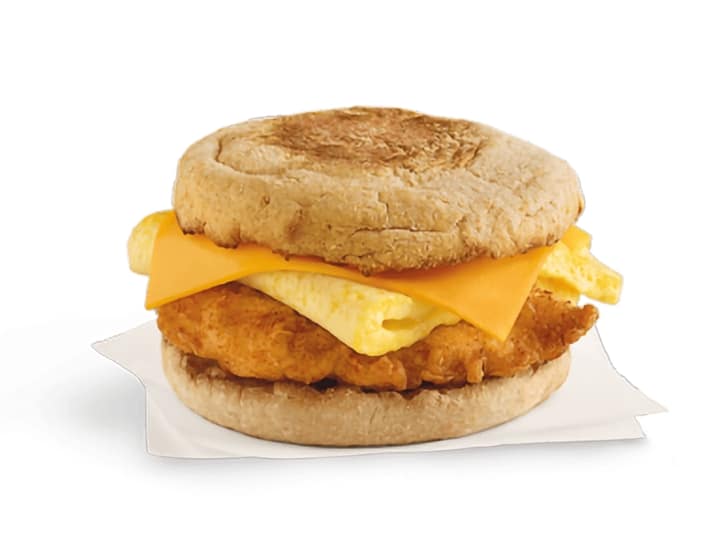 An english muffins with cheese, an egg, and breaded chicken.