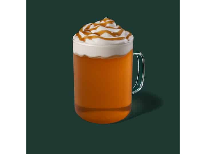 A clear cup of starbucks apple spice with whipped cream on top.