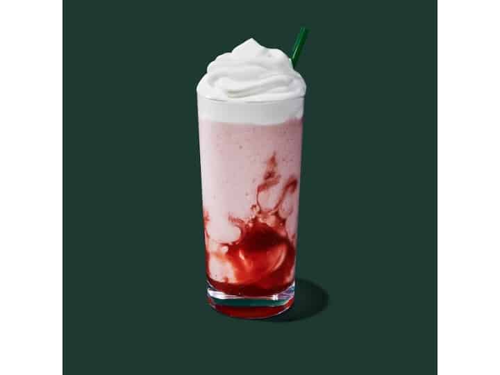 A glass cup of starbucks strawberry creme frappuccino with whipped cream on top.